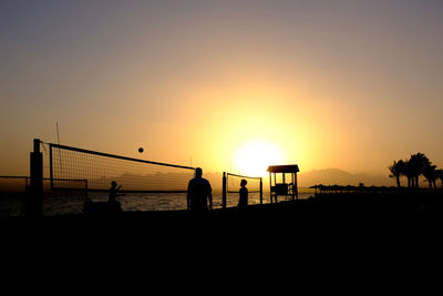 Silhouette people on beach against sky during sunset