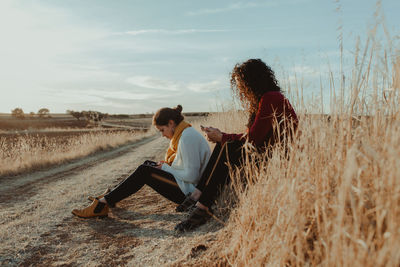 Women sitting on field against sky