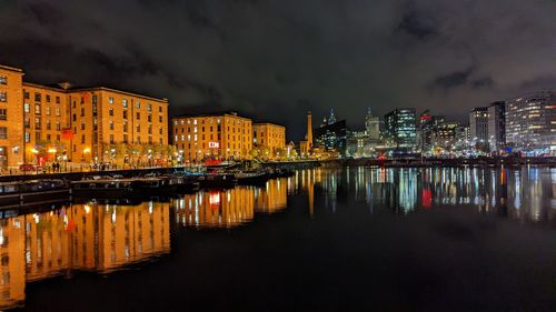 Illuminated buildings by river against sky at night