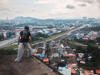 Rear view of man looking at cityscape against sky