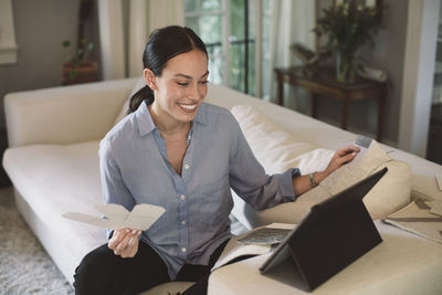 Smiling designer holding labels while looking at laptop in home office