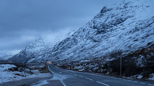 Empty road amidst snowcapped mountains against sky