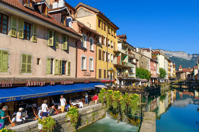 People on canal amidst buildings in city against sky