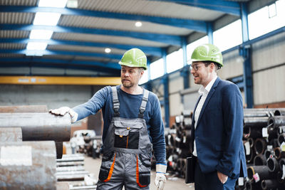 Warehouse worker discussing over pipe with male manager in industry