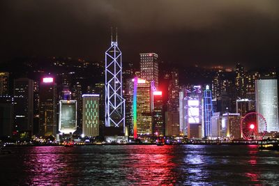 Illuminated buildings by river against sky at night