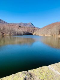 Scenic view of lake by mountains against clear blue sky