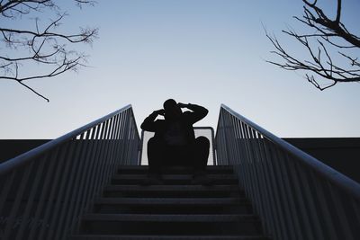 Low angle view of silhouette man sitting on steps against sky
