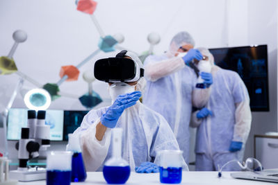 Scientist wearing virtual reality simulator colleague in background at laboratory