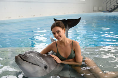 Young woman in bikini while standing by dolphin swimming pool