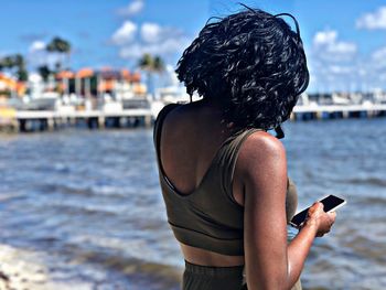 Rear view of woman using mobile phone at beach