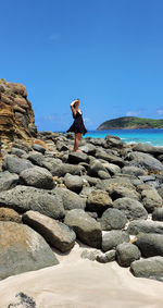 Rear view of man sitting on rock against clear sky