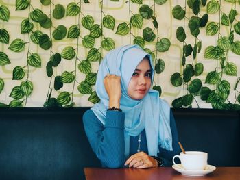 Portrait of young woman wearing hijab while sitting at table in restaurant