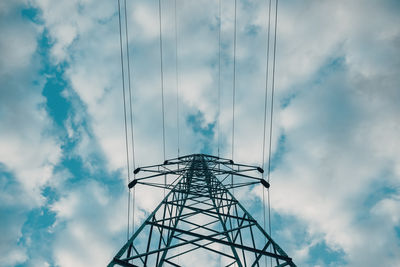 Electricity pylon with overhead powerline cables against cloudy sky, low angle view