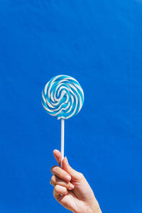Crop hand of unrecognizable female with delicious lollipop on stick against blue wall in city on sunny day