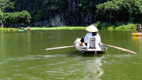 Rear view of woman on boat with asian style conical hat in river during sunny day