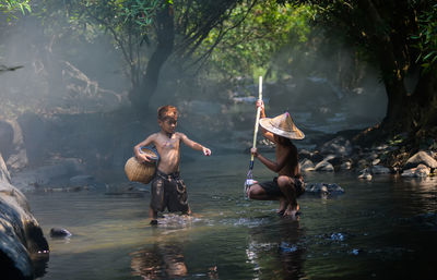 Shirtless brothers fishing in river at forest