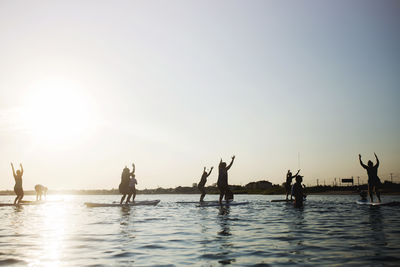 People on water against clear sky during sunset