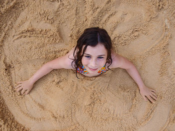 High angle portrait of smiling girl lying on sand at beach