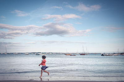 Girl running at beach against cloudy sky