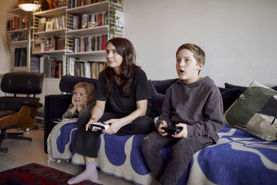 Mother with sons sitting on sofa and playing video games