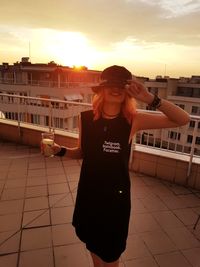 Woman holding drink while standing on terrace in city against sky