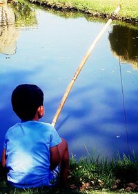 Rear view of boy sitting by lake