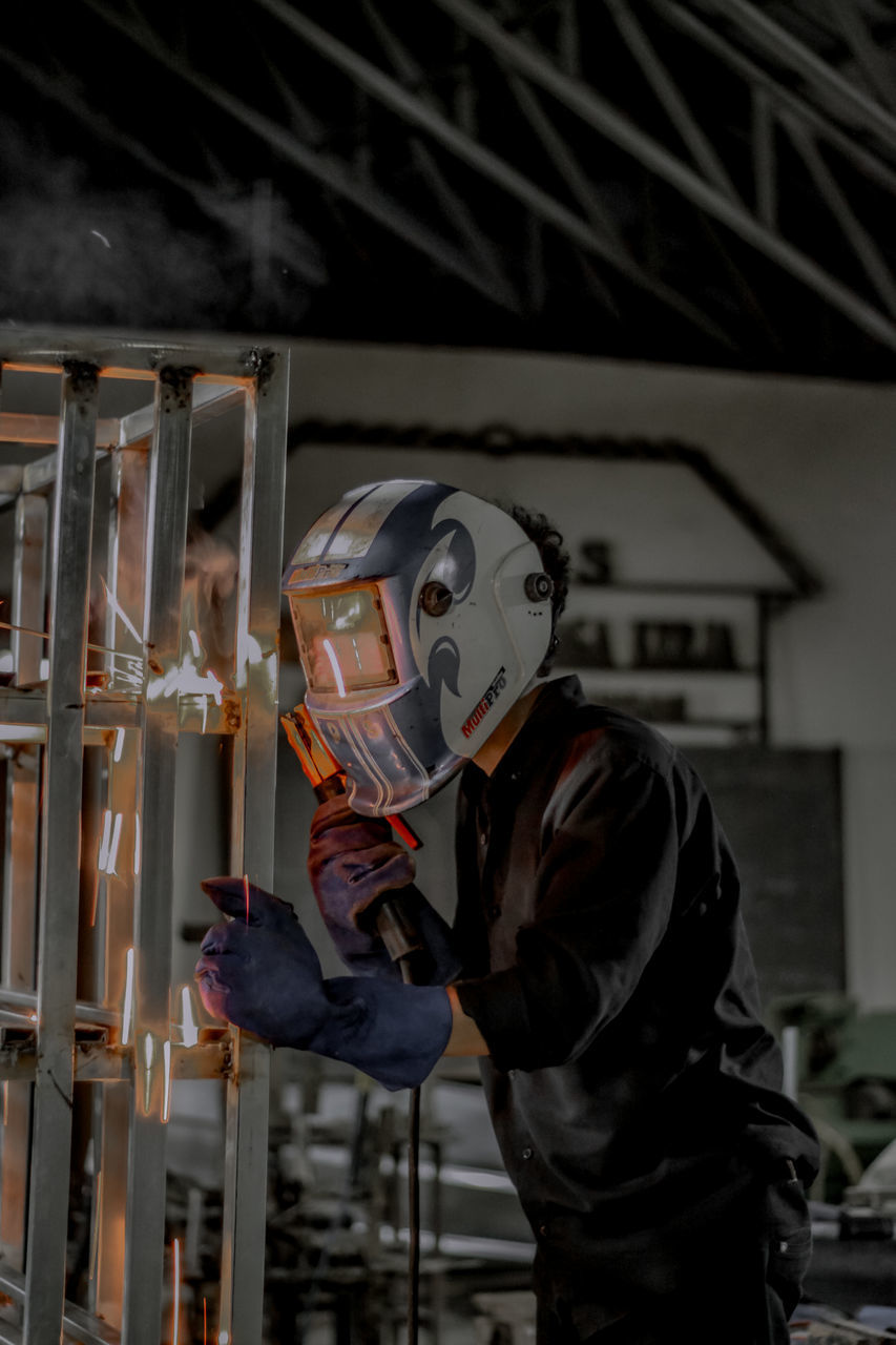 occupation, one person, protection, protective workwear, adult, industry, helmet, indoors, working, headwear, men, security, manual worker, clothing, person, skill, standing, mask, waist up, metal industry, protective mask - workwear, welder, holding, three quarter length
