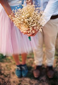 Low section of couple holding flower while standing on field