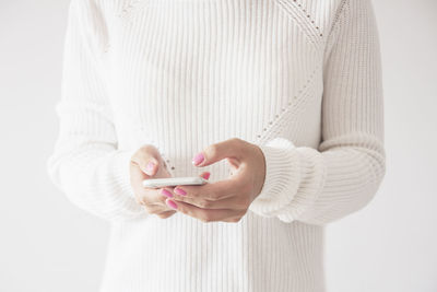 Midsection of woman holding mobile phone against white background