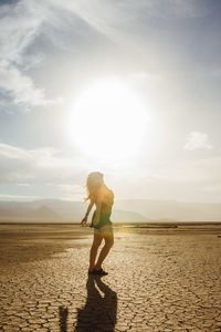 Side view of young woman standing at desert against sky during sunny day
