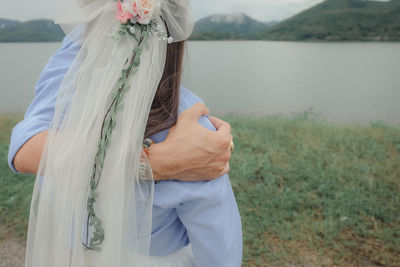 Midsection of woman standing on field by lake