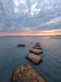 Rocks on sea shore against sky during sunset