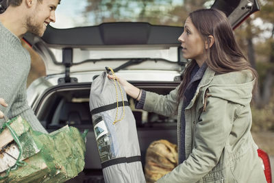 Side view of couple holding camping equipment against car