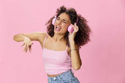 Portrait of young woman standing against pink background