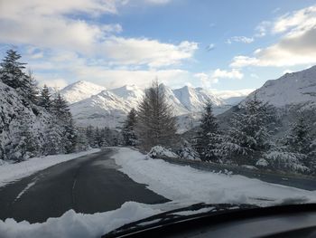 Road by snowcapped mountains against sky seen through car windshield