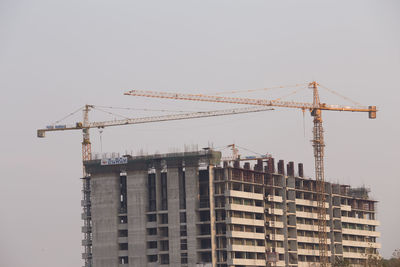 Low angle view of cranes on building against sky