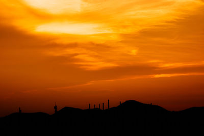 Silhouette people on land against dramatic sky during sunset