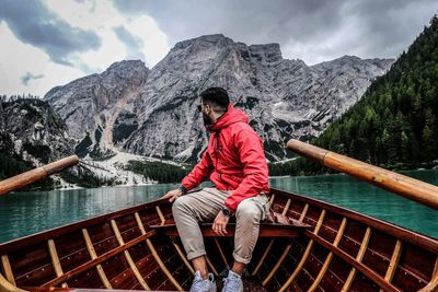 Man sitting on boat in lake against mountains and sky