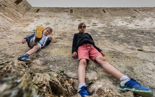 Low angle view of siblings standing on rock by building