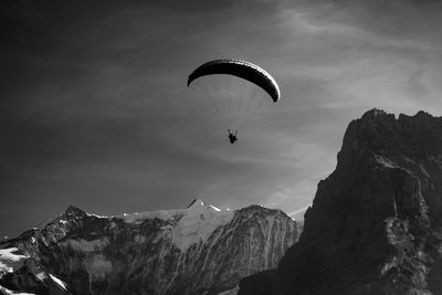 Person paragliding over mountains against sky