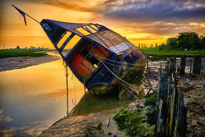 Abandoned boat in sea against sky during sunset