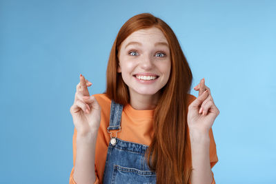 Excited woman with fingers crossed against blue background