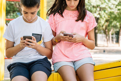 Siblings using phones while sitting outdoors