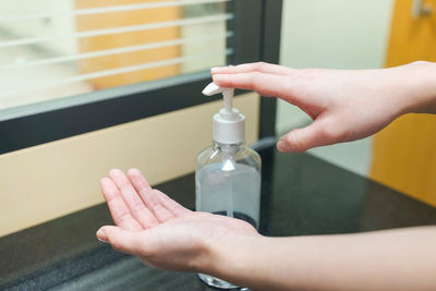 Close-up of woman hand holding glass bottle against window