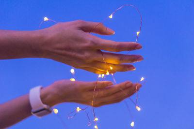 Close-up of hand holding lit candle against sky