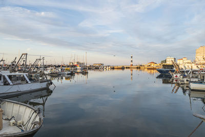  the port of cattolica with the boats and the lighthouse reflecting in the water at sunset