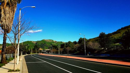 Road by trees against blue sky