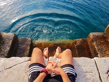 Low section of people sitting by sea