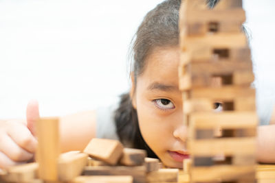 Close-up portrait of girl playing block removal game on table against wall