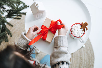 Crop photo of young woman in nordic sweater packing gift box at home